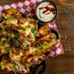 A plate of TGI Friday's-style potato skins, generously topped with melted cheddar cheese, crispy bacon bits, a dollop of sour cream, and a sprinkle of fresh green onions.